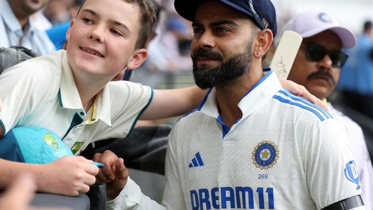 Virat Kohli wearing a black arm band takes a photo with a kid