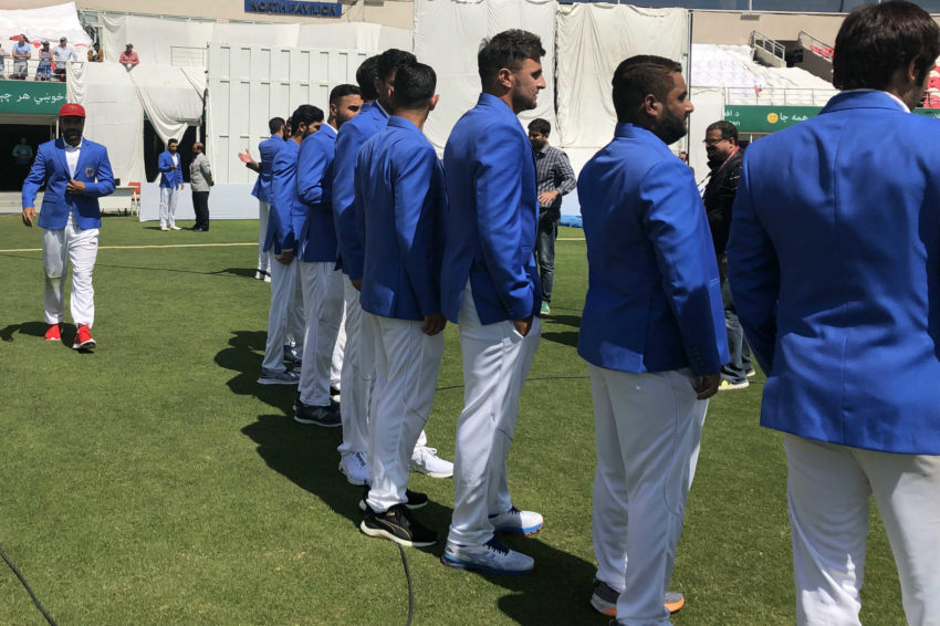 Rashid Khan in shiny blue team blazer, red Test cap, and the matching shoes. 